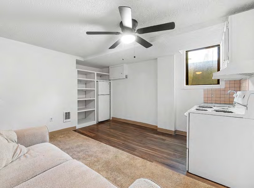 Interior view of a living area with a ceiling fan, kitchen appliances, and shelving